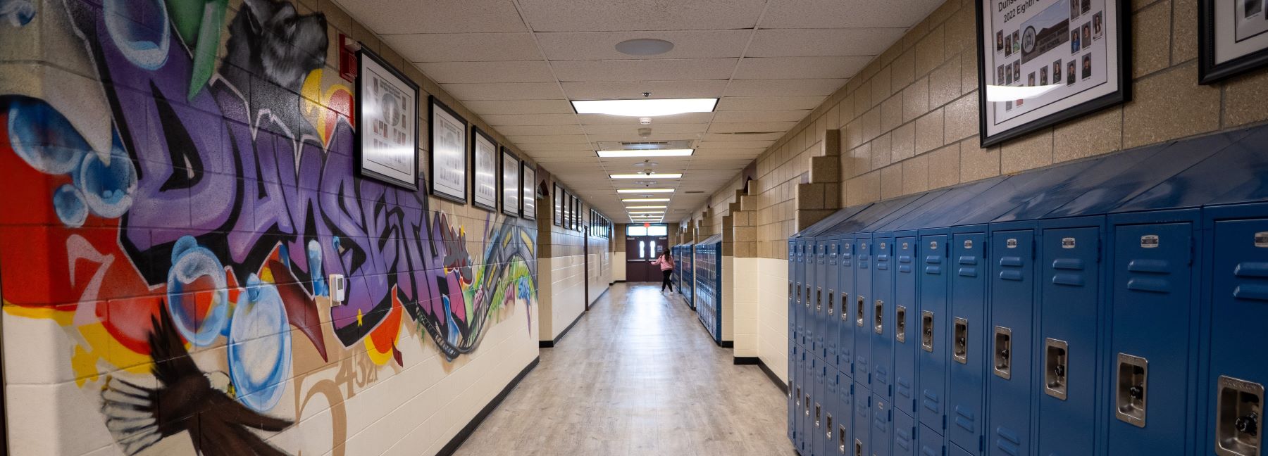 School hallway filled with colorful mural on the walls and metal lockers lining the sides.
