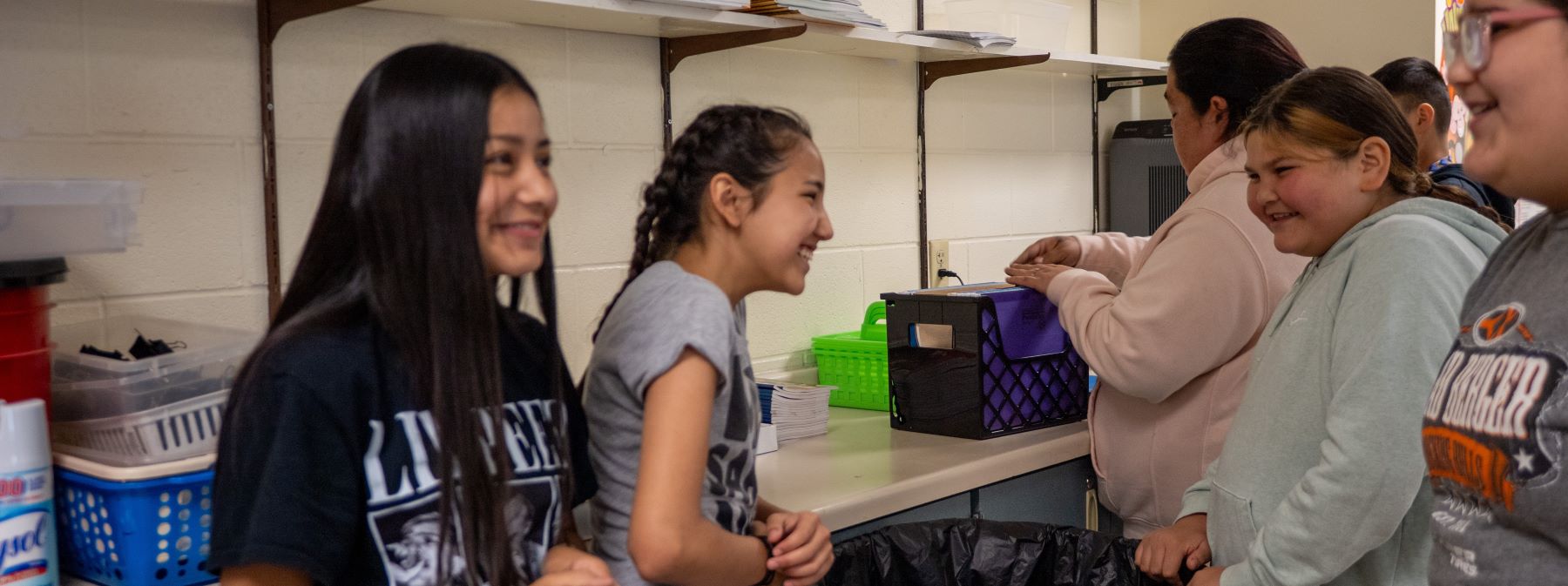 A group of students gathered around a table in a classroom, engaged in conversation and activities.