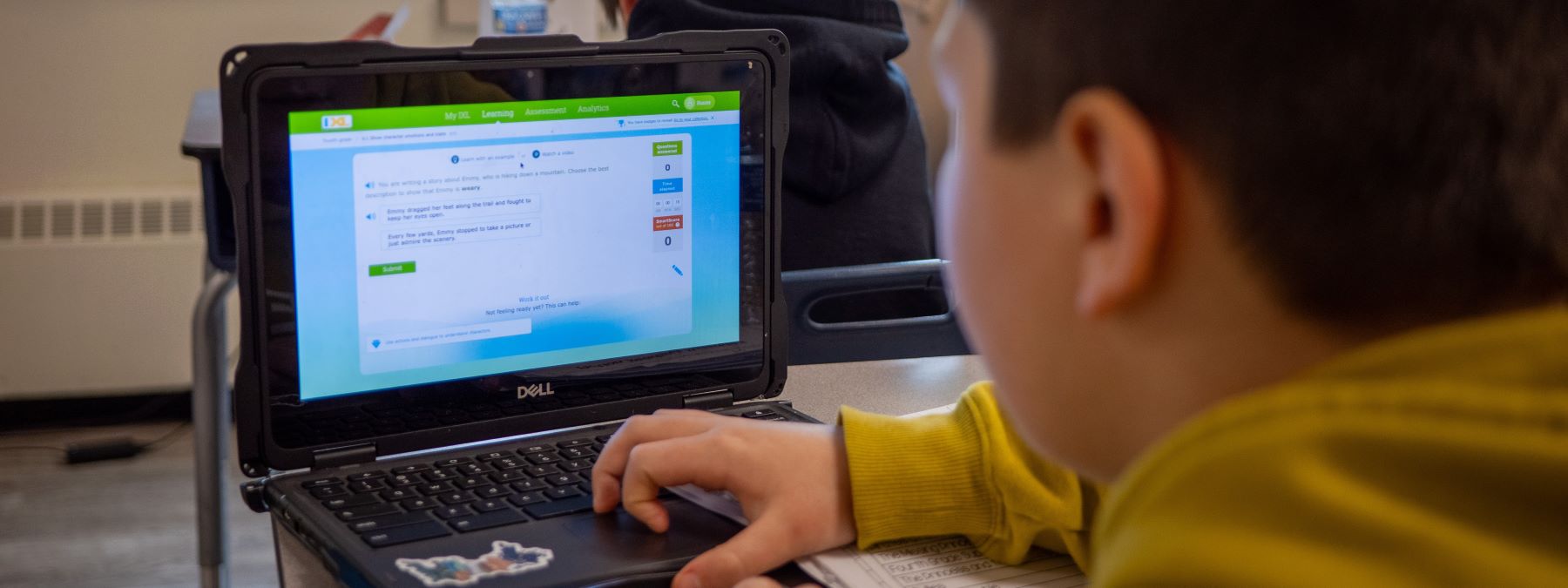 A young student focused on a laptop in a bright classroom, engaged in learning activities.