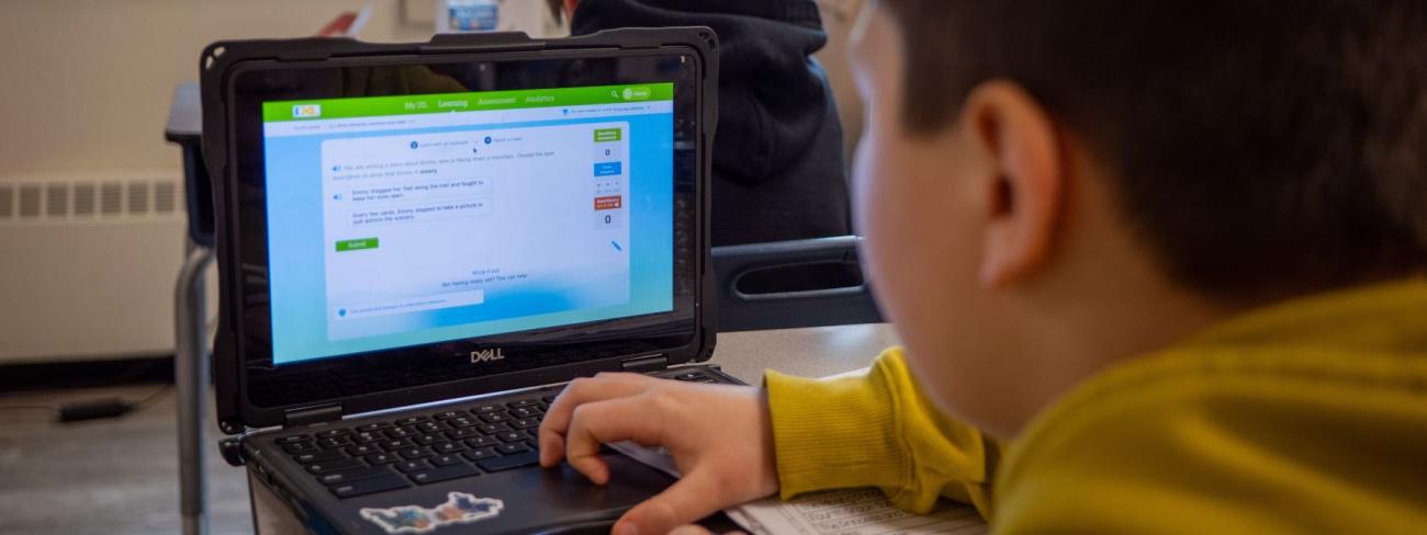 A young student focused on a laptop in a bright classroom, engaged in learning activities.
